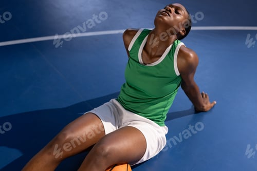 Preview: Resting on basketball court, female basketball player in green jersey relaxing
