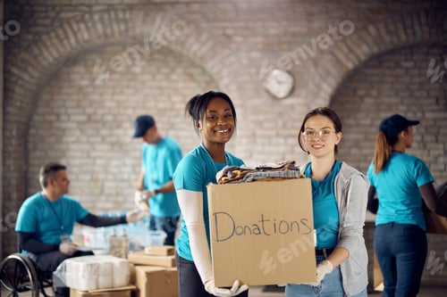 Preview: Happy female volunteers with donation dox at humanitarian aid center looking at camera.