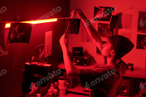 Preview: Side View of Teen Boy Hanging Photo Print On String to Dry in Darkroom