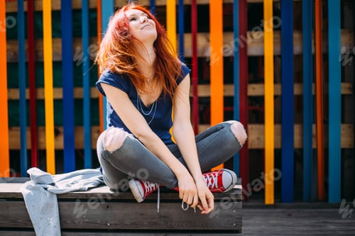 Preview: Bright red-haired girl teenager in jeans and sneakers on a colorful background
