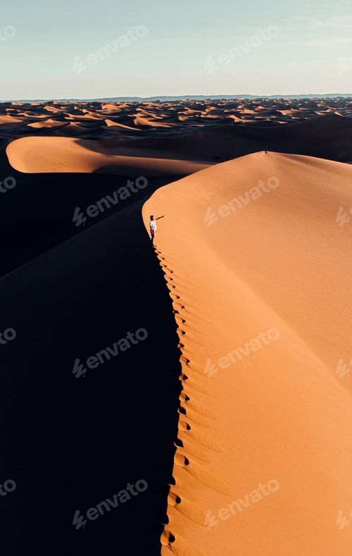 Preview: Vertical shot of a man standing on a sand hill in the desert