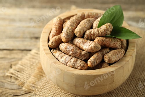 Preview: Tumeric rhizomes with leaves in bowl on wooden table, closeup