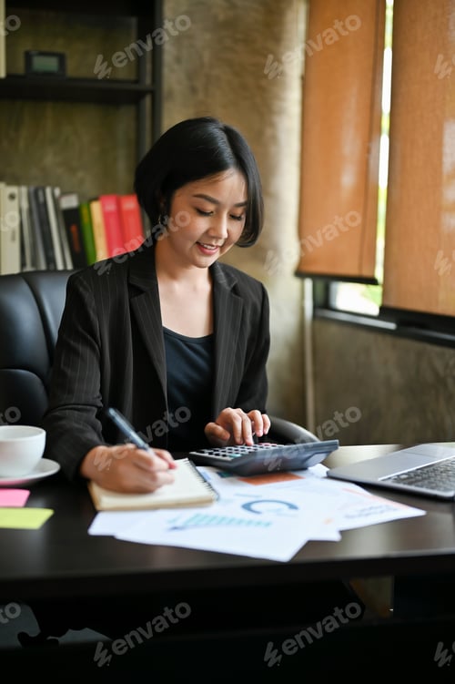 Preview: A beautiful Asian businesswoman calculates sales using a calculator and laptop