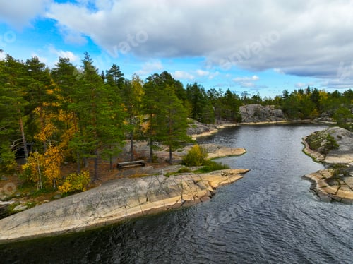 Preview: Rocky shore and pine trees beside a still, dark body of water