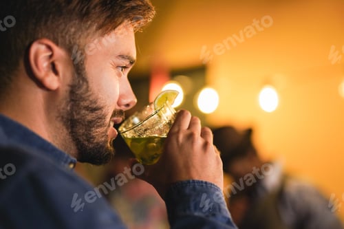 Preview: Young beautiful latin man drinking cocktail - Lights and peoples in background