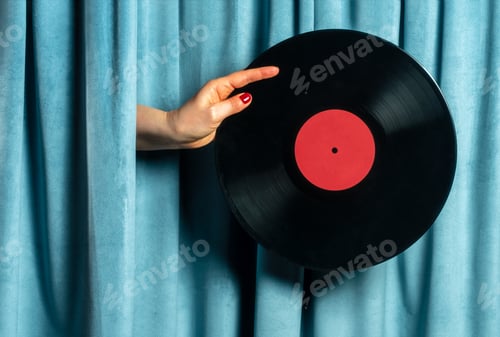 Preview: Female hand holds vinyl record on blue curtains background