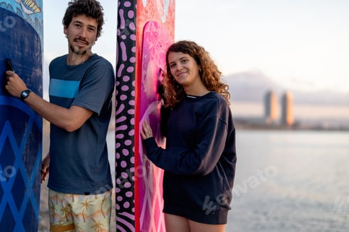 Preview: Friends share a joyful moment at the beach during sunset, holding vibrant surfboards while laughing
