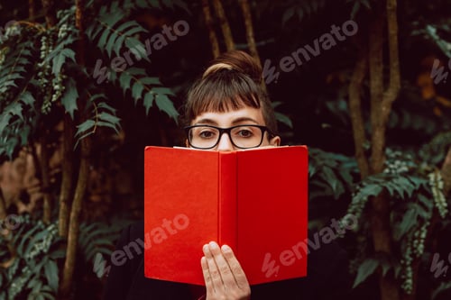 Preview: Young woman reading book on bench in park