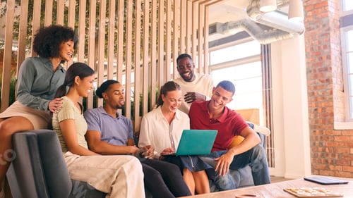 Preview: Multi-Cultural Business Team Sitting On Couch In Modern Open Plan Office Working On Laptop Together