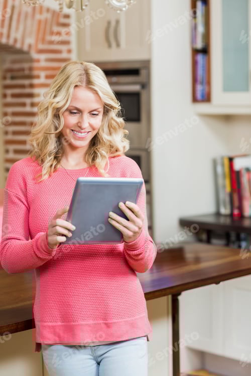 Preview: Leaning woman holding tablet and browsing recipes at home kitchen counter, showing cookbooks
