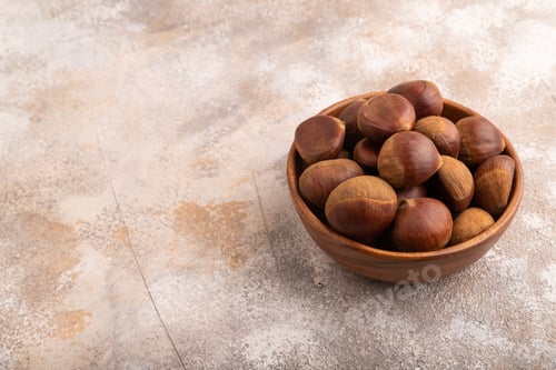 Preview: wooden bowl with raw edible Сhestnuts on brown concrete, side view, copy space, minimalism