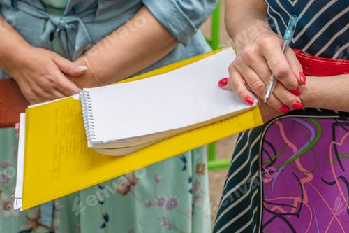 Preview: Cropped female hands hold a folder with papers, a notebook and a pen for notes.