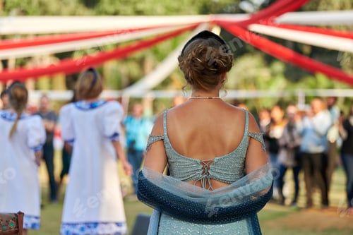 Preview: Back view of attractive woman in backless green dress looks at dancing performance at festival