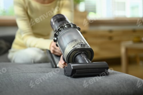 Preview: Closeup view of young woman cleaning sofa with cordless vacuum cleaner to removes germs and dirt.
