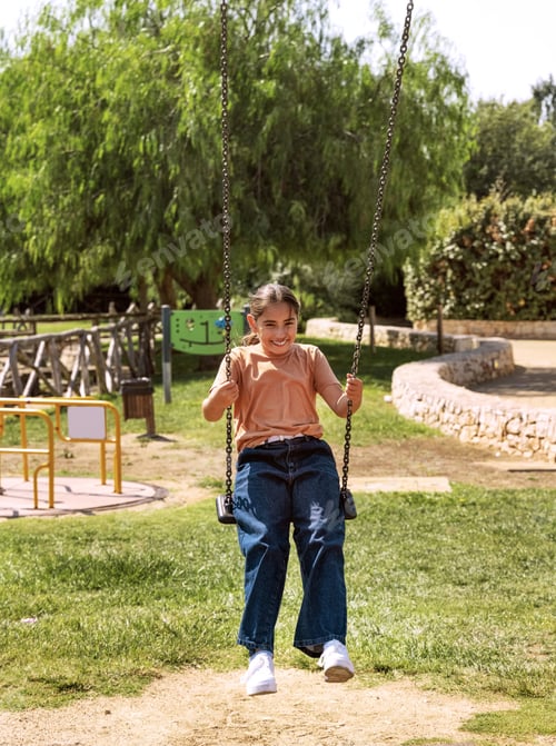 Preview: Happy kid girl having fun with chain swing on playground in a park