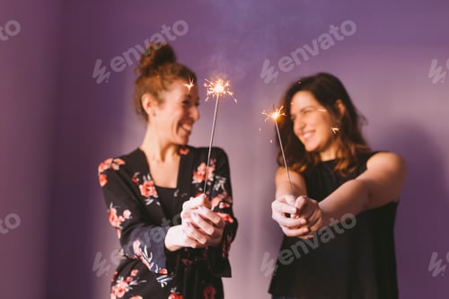 Preview: happy female friends holding sparklers indoors