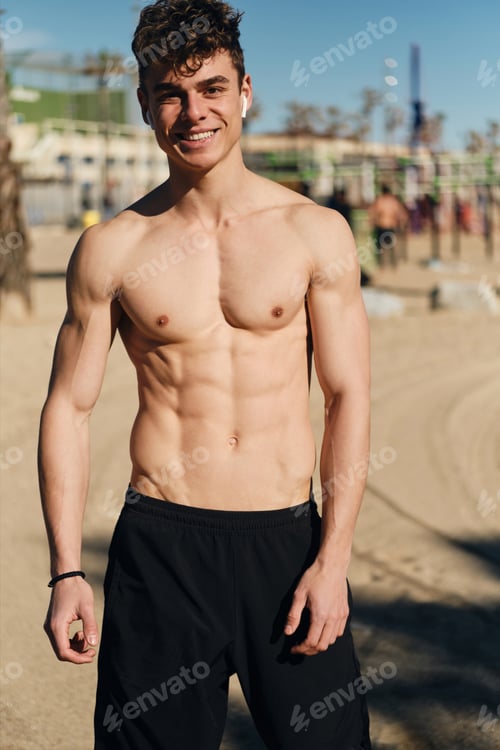 Preview: Young cheerful man with naked torso happily looking in camera after workout outdoor