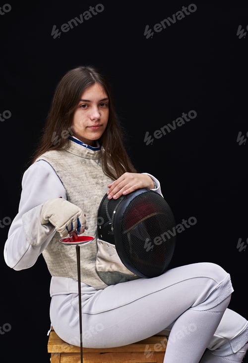 Preview: Portrait of woman dressed in white fencing costume practicing with the sword on black background.