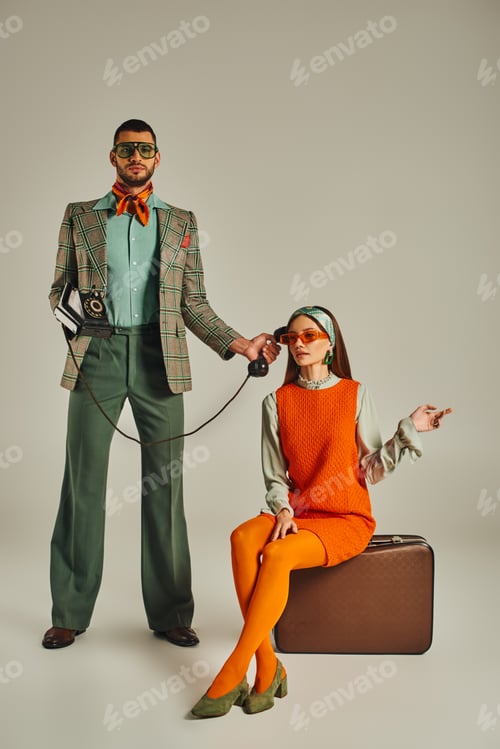 Preview: trendy man holding rotary phone near woman sitting on vintage suitcase on grey, retro lifestyle