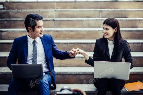 Preview: Young business couple sitting on staircase working some before go work on laptop.