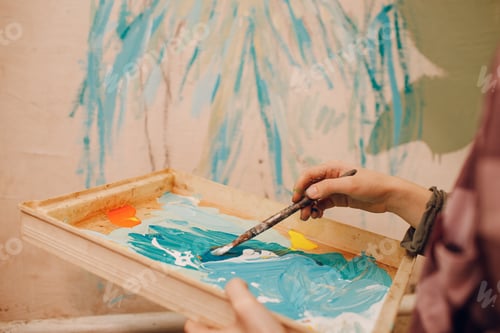 Preview: Young woman with a spray balloon with paint in her hand in a protective mask painting wall