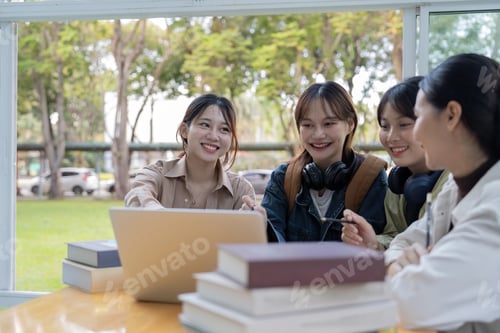 Preview: University students sitting together at table with book and laptop. Happy young people doing group