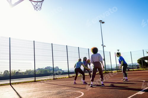 Preview: Diverse group of young woman having fun playing basketball outdoors.