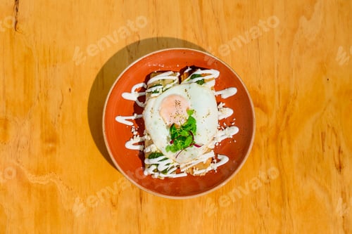 Preview: Top view of a fried egg with veggies and sauces on a plate on the table