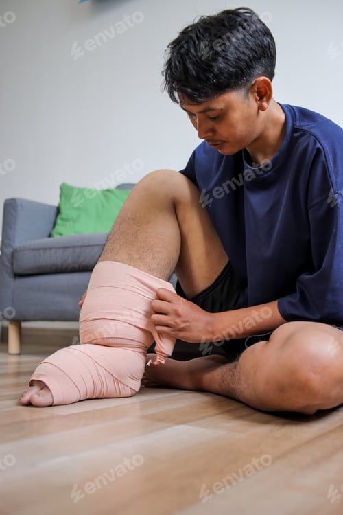 Preview: Young Asian Male With Lymphatic Filariasis Applying Self Care Bandage While Sitting On The Floor