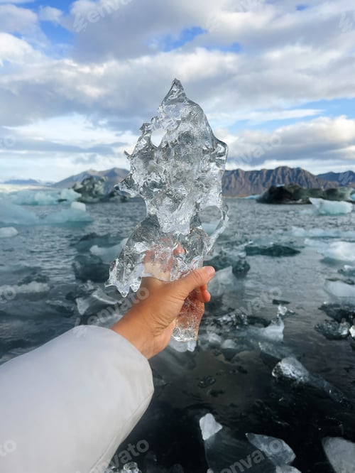 Preview: Female hand in blue jacket holding piece of ice in the glacier lagoon in Iceland