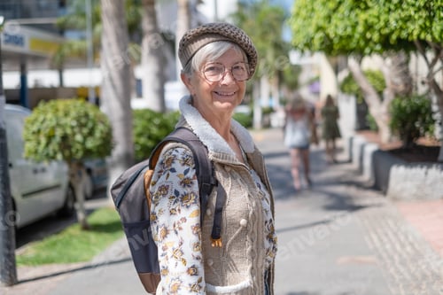 Preview: Smiling senior woman traveler in city centre expressing positivity, good mood, holding backpack