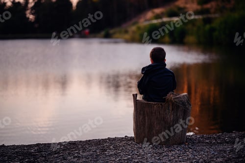 Preview: Boy Sitting on Tree Stump Gazing at Calm Lake