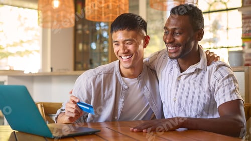 Preview: Same Sex Male Couple At Home With Laptop And Credit Card Booking Holiday Or Shopping Online