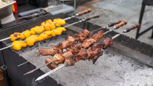 Preview: Grilled meat and vegetables on skewers cooking over charcoal