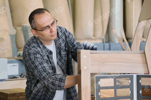 Preview: Male carpenter working in furniture joinery, master making wooden chair in wood workshop
