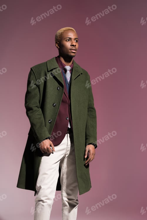 Preview: Fashionable young african man in cloak looking away on pink background