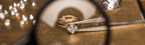 Preview: Selective focus of magnifying glass, jewelry ring with gemstone in tweezers on board, panoramic shot