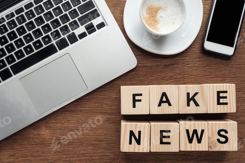 Preview: top view of wooden cubes with words fake news, laptop and cup of coffee on wooden tabletop