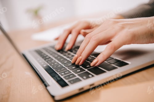 Preview: close up view of woman typing on laptop at wooden table