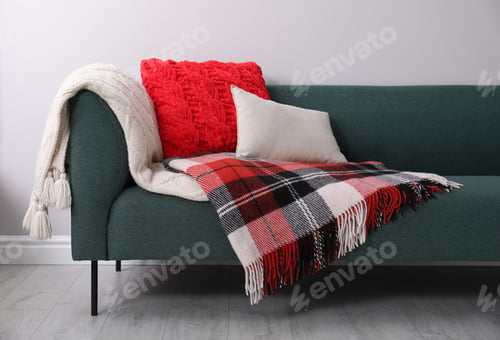 Preview: Sofa with soft pillows and warm plaids near light wall indoors