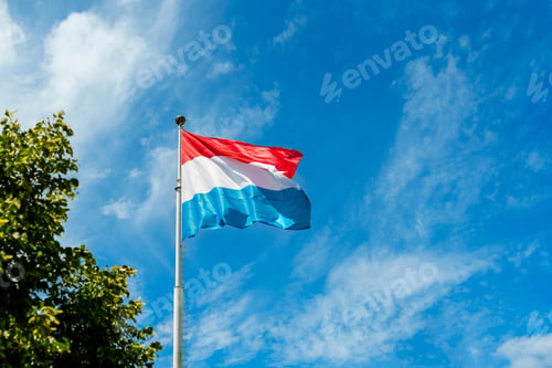 Preview: Flag of Luxembourg blowing in the wind against a blue sky with white clouds