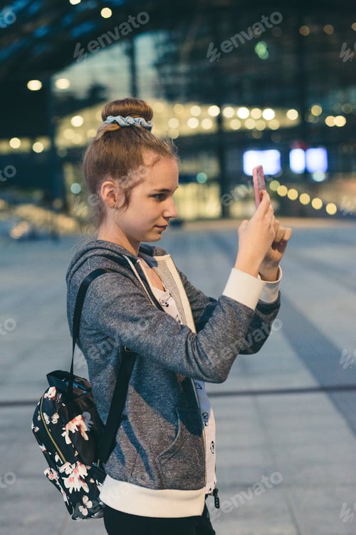 Preview: Young woman taking photos using a smartphone in the city at night