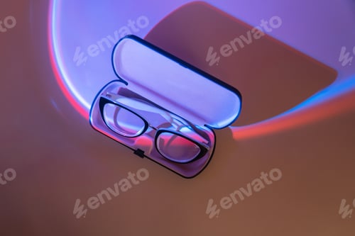 Preview: Folded vision glasses with black frames in a light case under blue light