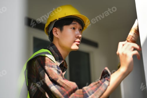 Preview: Professional painter in safety helmet holding brush in hand and paint the wall.