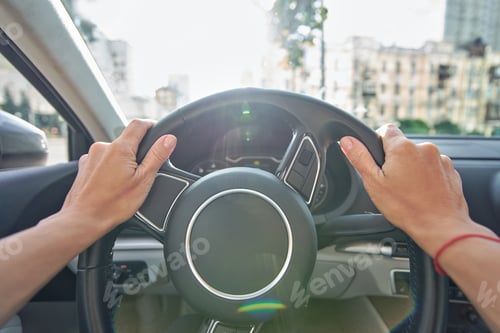 Preview: Woman driving through the city streets, close up shot of female hands on steering wheel