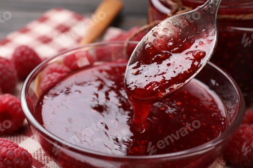 Preview: Taking sweet raspberry jam with spoon from glass bowl on table, closeup