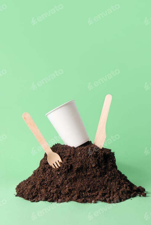 Preview: Paper cup and wooden fork, knife in heap of soil on green background
