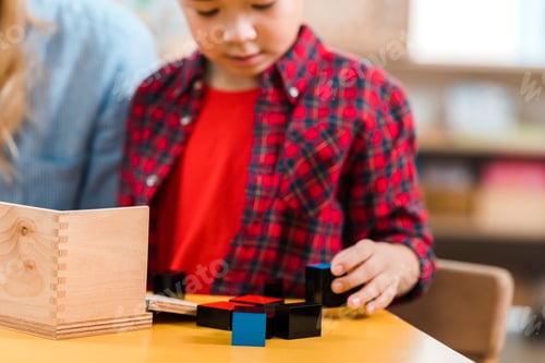 Preview: Selective focus of kid playing building blocks beside teacher in montessori school