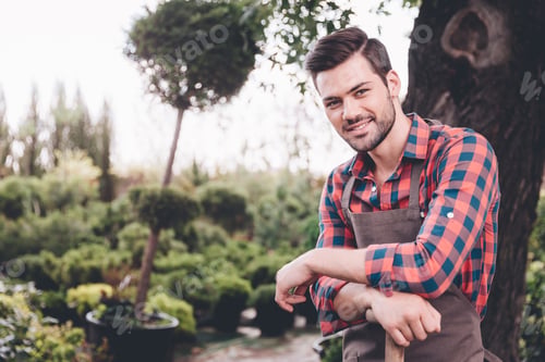 Preview: portrait of young smiling gardener in apron looking at camera in garden