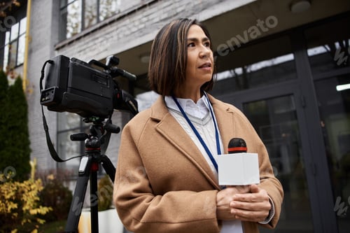 Preview: Multiracial female journalist in beige coat reports live from an outdoor news location